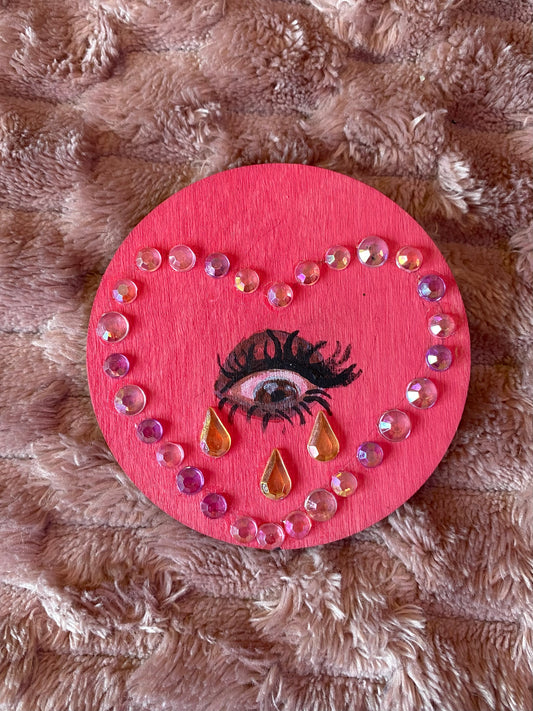 pink round magnet with an eye inside a heart crying gemstones. 