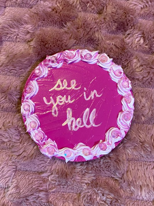 round disc decorated like a cake with "see you in hell" written in the center