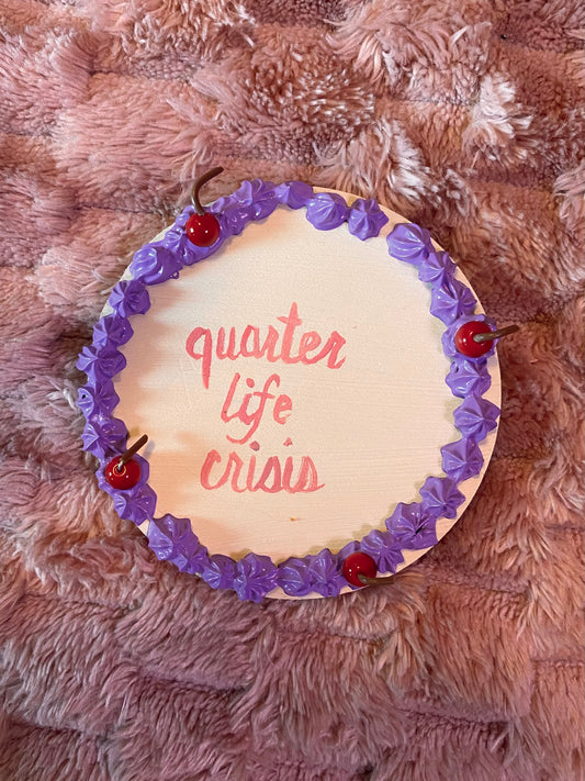 round disc decorated like a cake with "quarter life crisis" in the middle